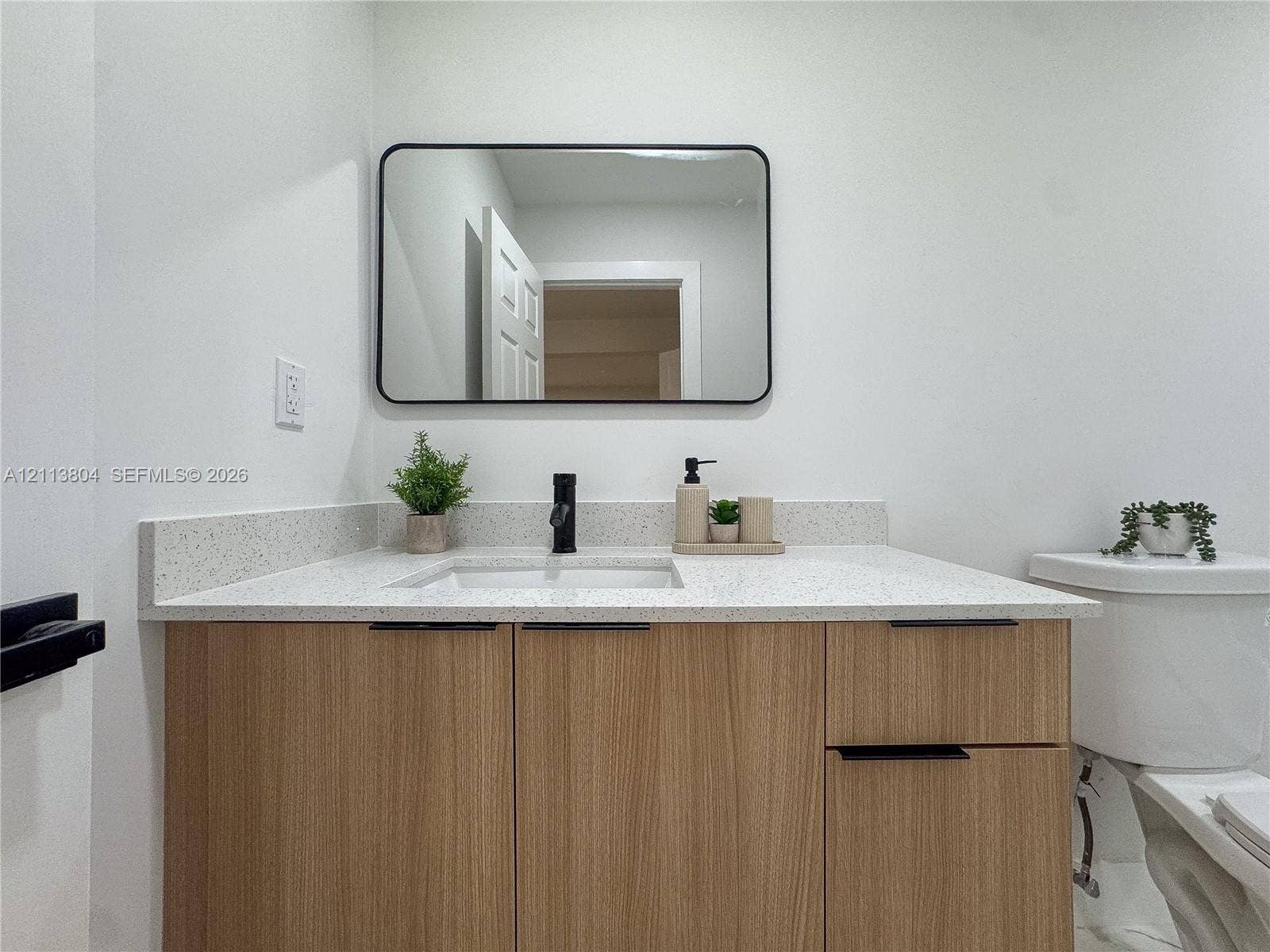 2300 NW 31st Avenue, Fort Lauderdale, FL 33311 Wood-finish cabinetry featuring black hardware, quartz-composite countertop, undermount sink, matte black faucet, and rectangular black-framed vanity mirror