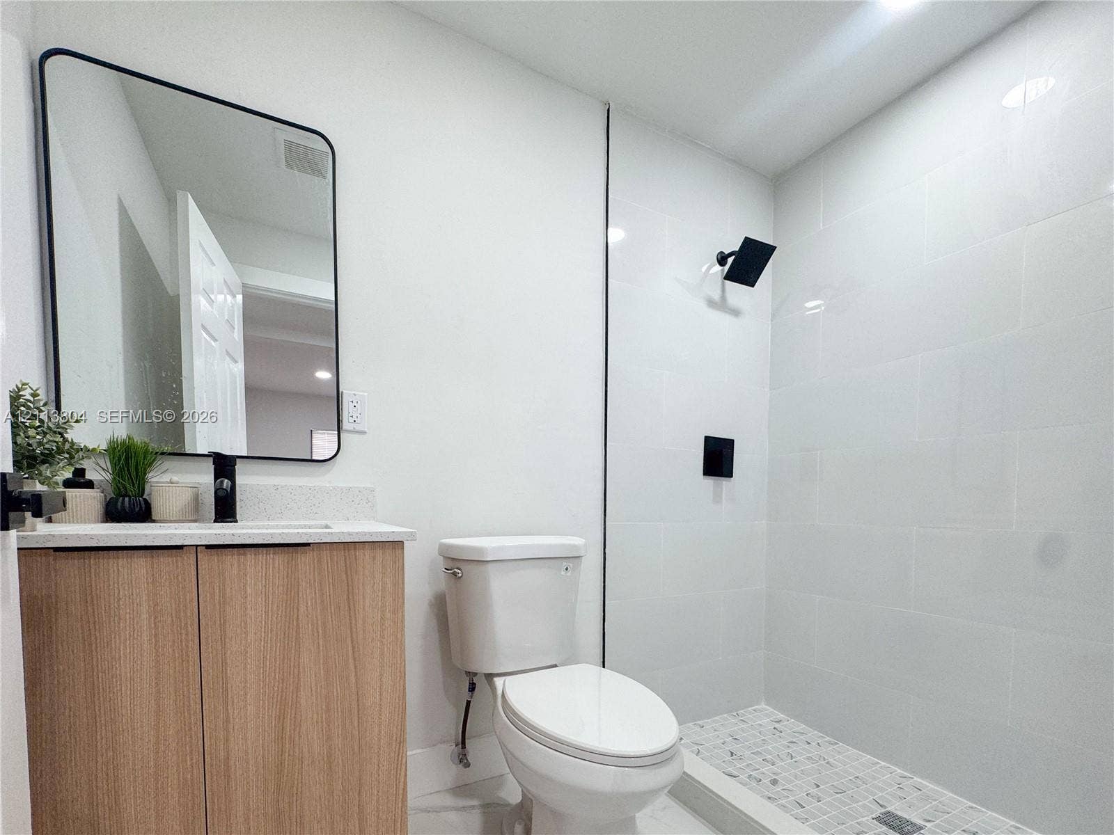 2300 NW 31st Avenue, Fort Lauderdale, FL 33311 Modern vanity featuring light wood-finish cabinetry, a stone-composite countertop, and a rectangular mirror with a black frame