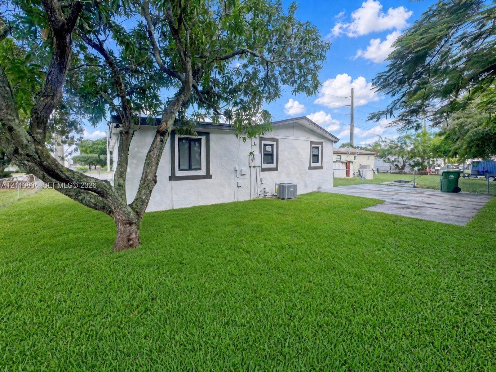 2300 NW 31st Avenue, Fort Lauderdale, FL 33311 Exterior featuring a light-toned textured finish, concrete patio, expansive lawn, and mature trees