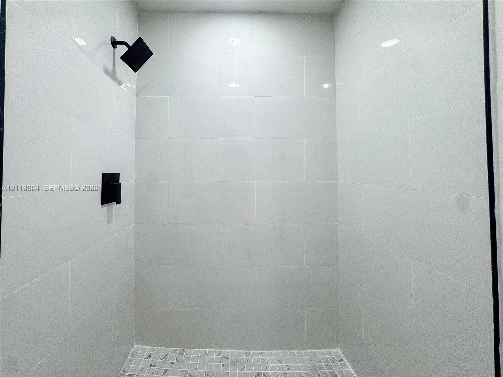 2300 NW 31st Avenue, Fort Lauderdale, FL 33311 Walk-in shower enclosure featuring white subway tile wall surround, matte black rainfall showerhead, matte black pressure-balance valve, and a mosaic tile floor