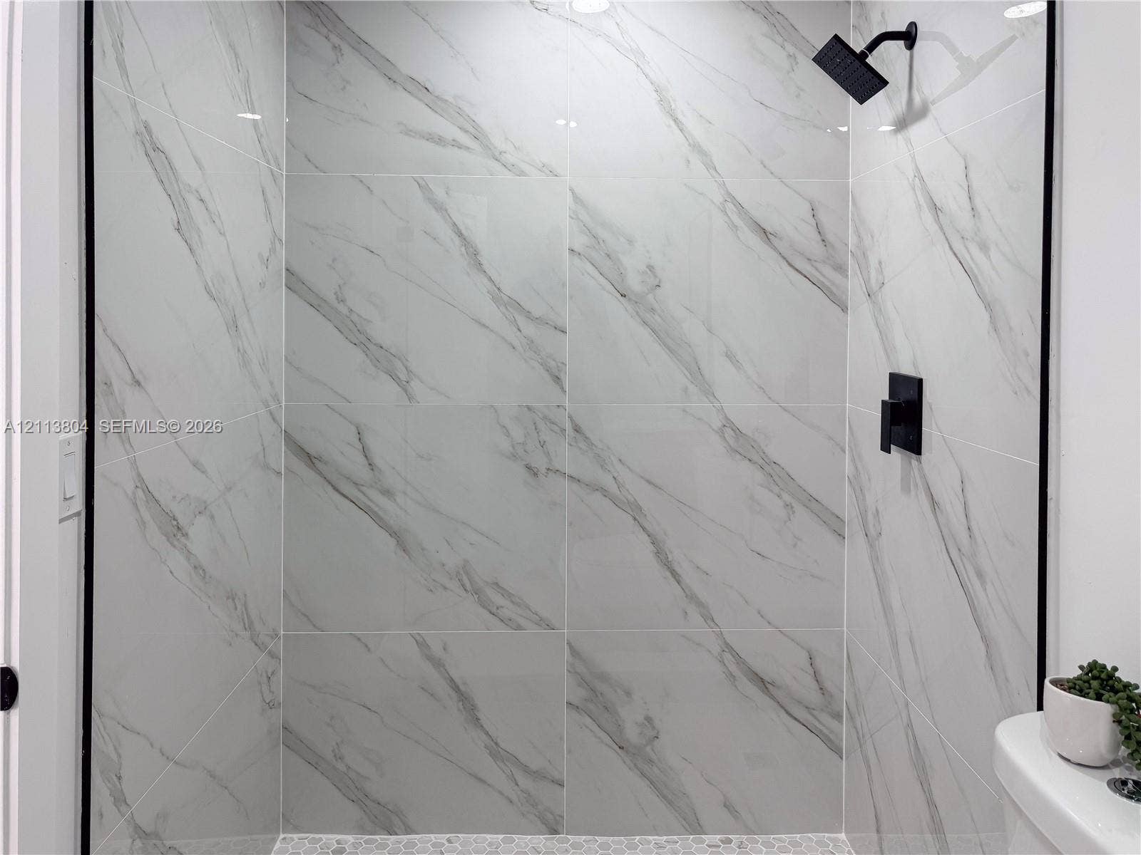 2300 NW 31st Avenue, Fort Lauderdale, FL 33311 Shower featuring floor-to-ceiling large-format tile with decorative veining, matte black wall-mounted shower head, matte black single-handle mixing valve, and stone hexagon mosaic floor tile