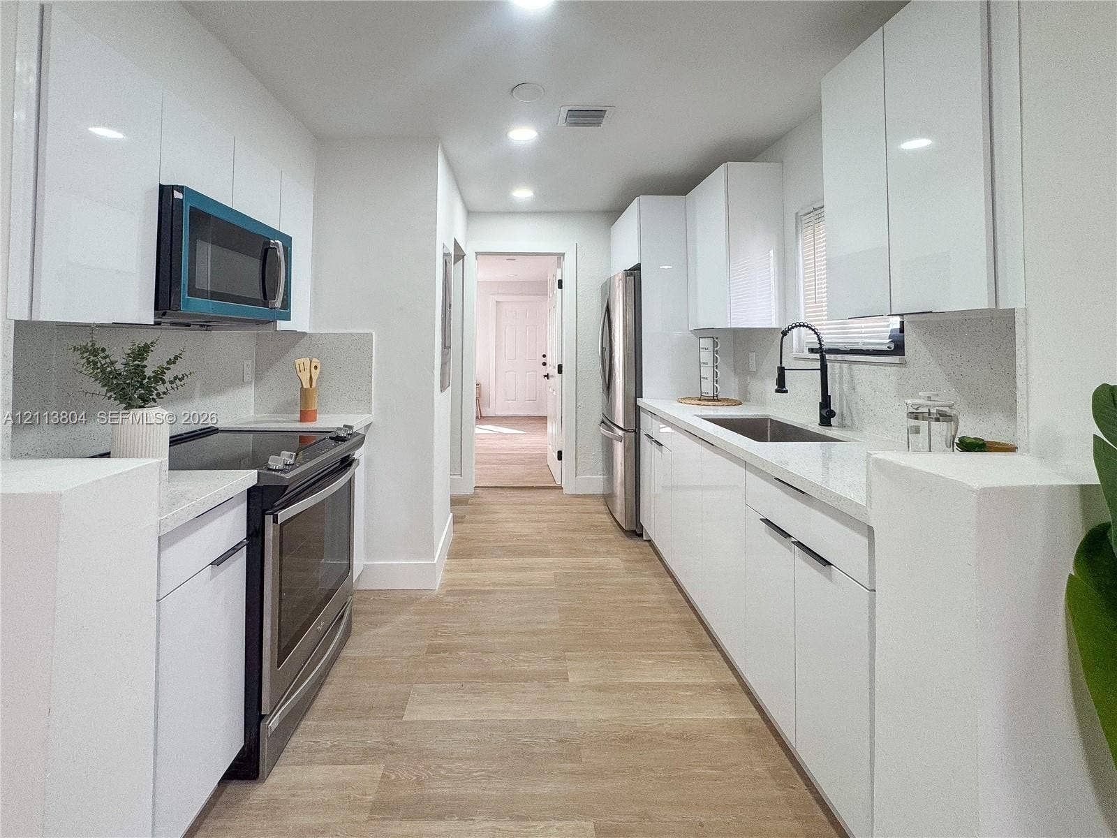 2300 NW 31st Avenue, Fort Lauderdale, FL 33311 Kitchen featuring high-gloss white cabinetry, white stone-finish countertops, stainless steel appliances, wood-finish flooring, and a matte black gooseneck faucet