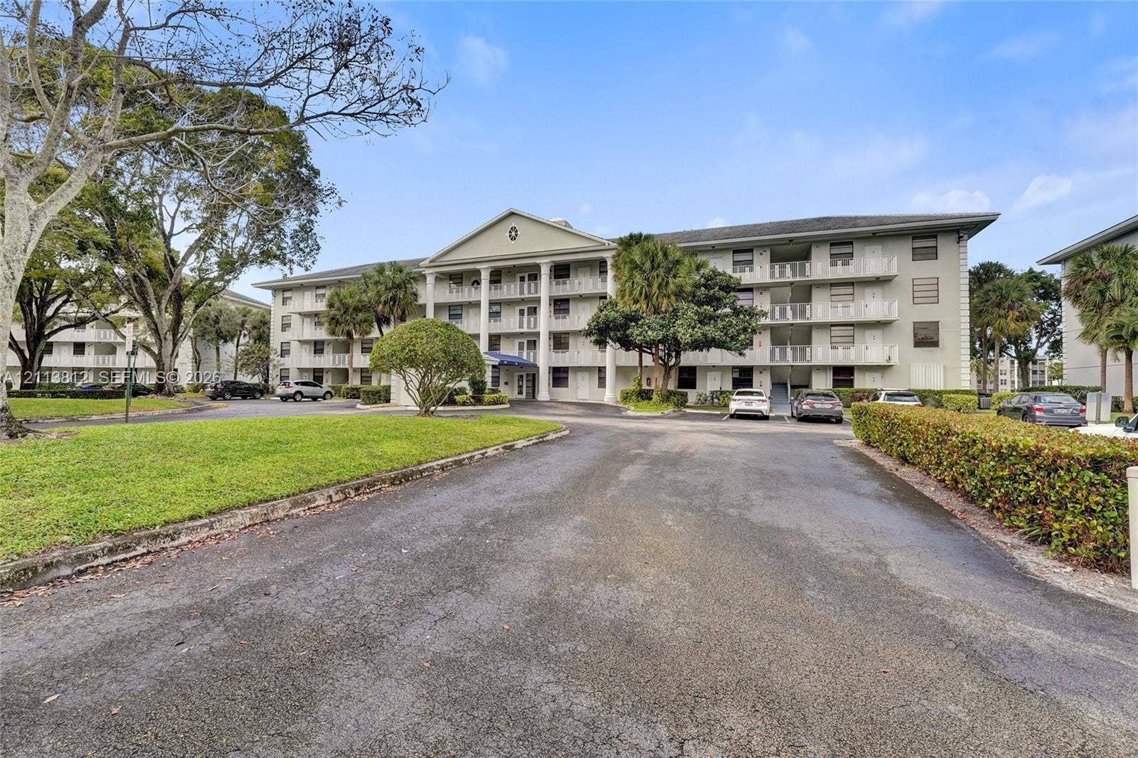 1516 Whitehall Drive, #204, Davie, FL 33324 Multi-story building exterior featuring a classical pediment, columned entryway, private balconies, and manicured landscaping