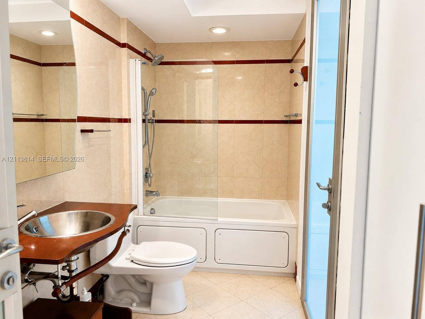 110 Washington Avenue, #1517, Miami Beach, Miami Beach, FL 33139 Bathroom featuring full-height neutral wall tiling with dark accent banding, a wood-surround vanity with a circular metallic vessel sink, a white drop-in soaking tub, and a glass shower panel