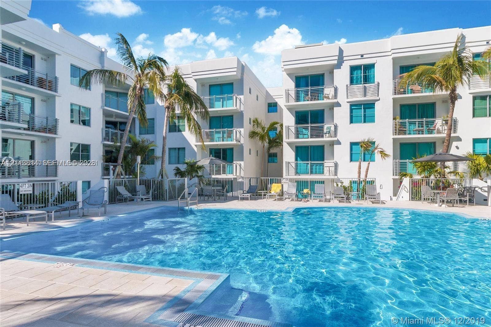 110 Washington Avenue, #1517, Miami Beach, Miami Beach, FL 33139 Swimming pool with light-colored tile decking, surrounded by multi-story white stucco building facades featuring private balconies with metal railings and palm landscaping