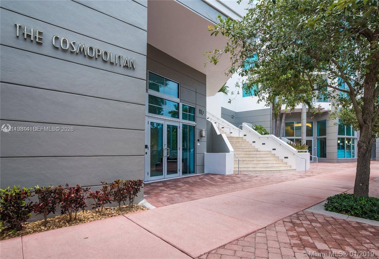 110 Washington Avenue, #1517, Miami Beach, Miami Beach, FL 33139 Building entrance featuring a multi-story facade, glass-paned double doors, stone staircase with metal railings, and patterned paver walkway