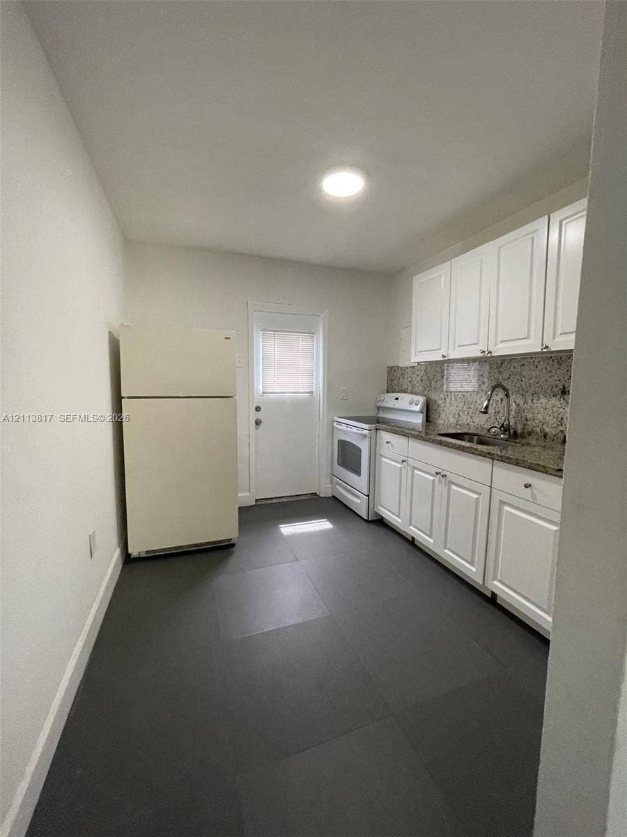 2515 NW 52nd Street, #1, Miami, Miami, FL 33142 Kitchen featuring white cabinetry, stone-finish countertops, dark large-format tile flooring, a stainless steel sink with a high-arch faucet, and an exterior door