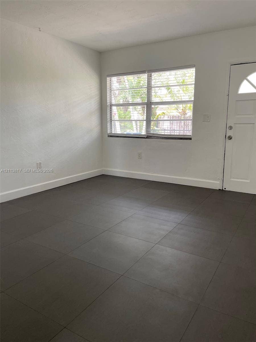 2515 NW 52nd Street, #1, Miami, Miami, FL 33142 Neutral-toned tile flooring, white wall finish, multi-pane window, and exterior door with a crescent-shaped glass inset