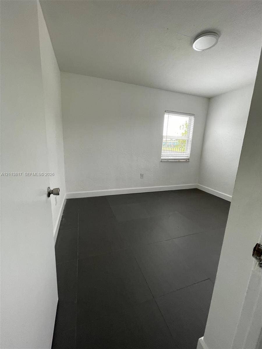 2515 NW 52nd Street, #1, Miami, Miami, FL 33142 Interior room featuring dark large-format tile flooring, white wall finishes, a single-pane window with horizontal blinds, and a flush-mount ceiling light fixture