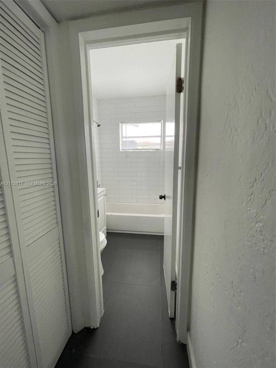 2515 NW 52nd Street, #1, Miami, Miami, FL 33142 Bathroom featuring large-format dark floor tile, white subway tile shower surround, and louvered-style closet doors