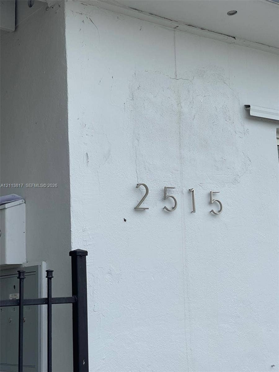 2515 NW 52nd Street, #1, Miami, Miami, FL 33142 Exterior wall featuring smooth white stucco finish, brushed metal house numbers, and black metal fencing