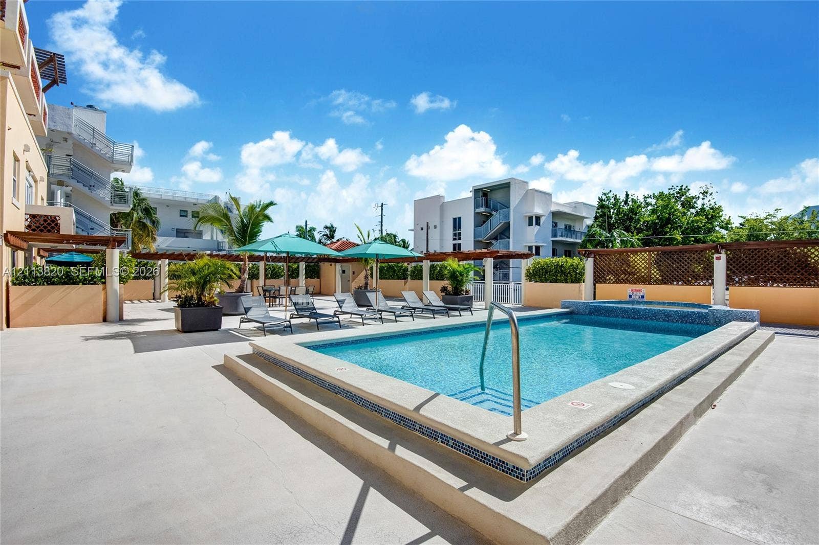 Outdoor pool featuring tiled edging and a built-in spa, expansive concrete pool deck, and wooden pergola covering