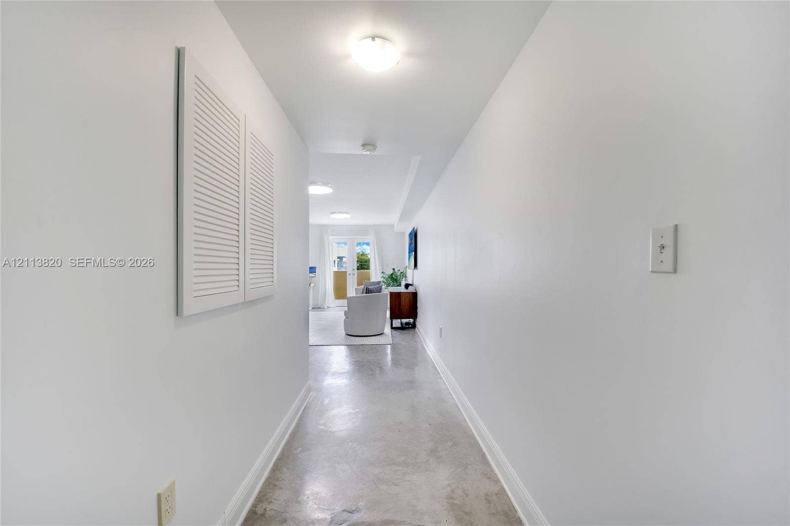 Hallway featuring polished concrete flooring, white walls, louvered closet doors, and flush-mount ceiling lighting