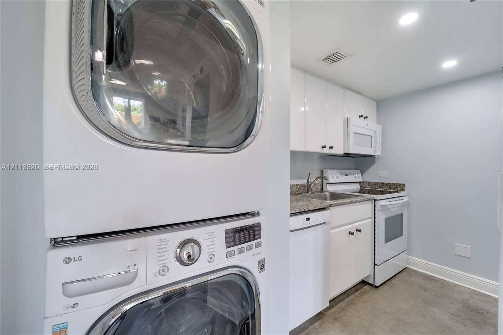 Laundry area featuring a stackable washer and dryer, white cabinetry, stone-finish countertops, stainless steel sink with a high-arch faucet, and white appliances