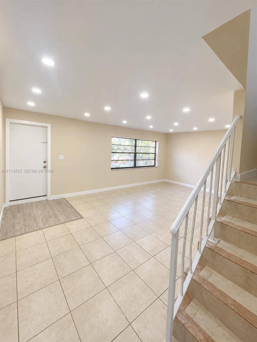 61 Matador Lane, #4-26, Davie, Davie, FL 33324 Open-concept interior featuring light-toned tile flooring, recessed ceiling lighting, a multi-pane window, and a staircase with a white metal railing