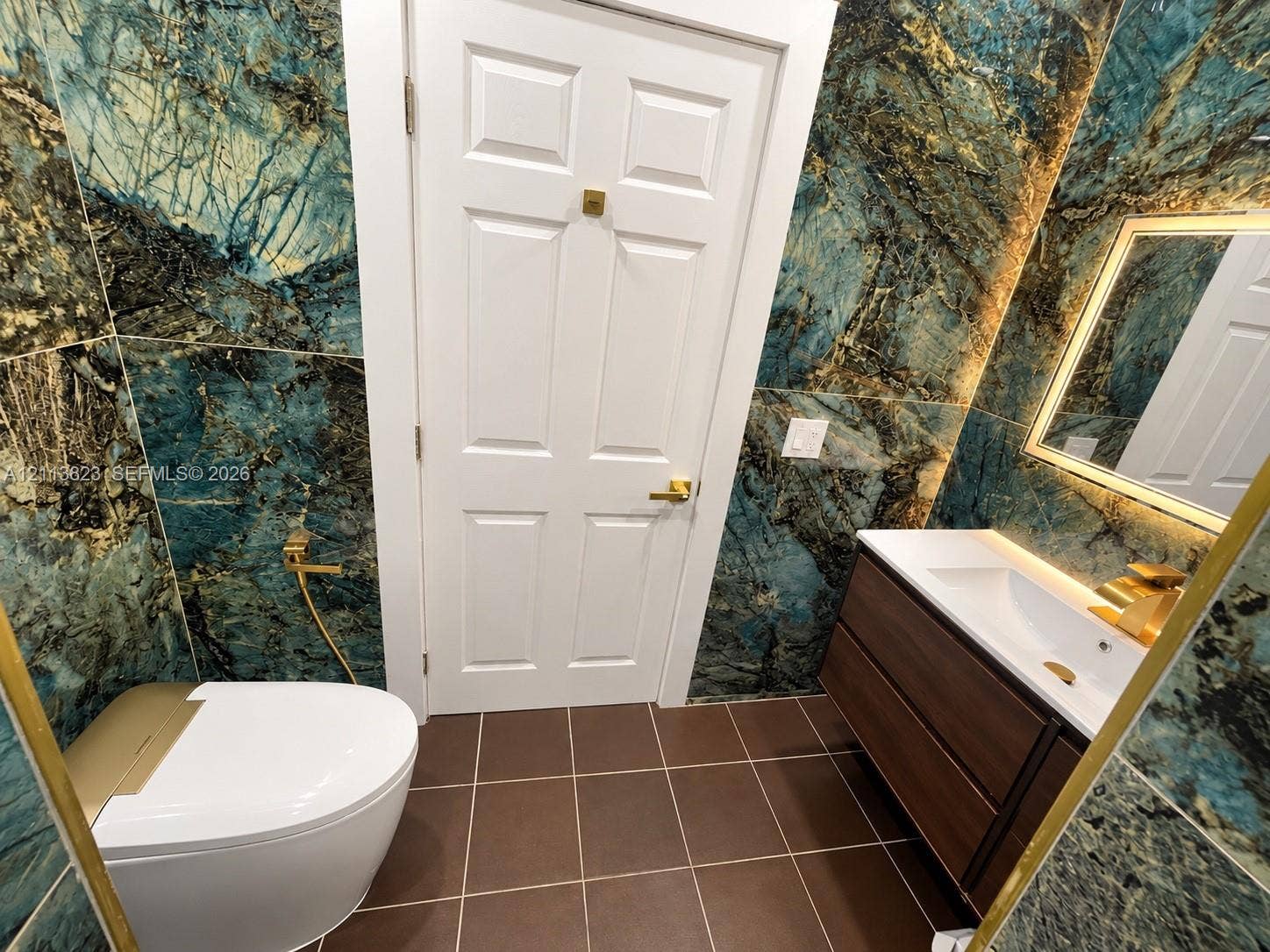 61 Matador Lane, #4-26, Davie, Davie, FL 33324 Full-height dark stone-patterned wall tiling, floating vanity with integrated rectangular sink, gold-tone hardware, backlit wall mirror, and modern low-profile toilet