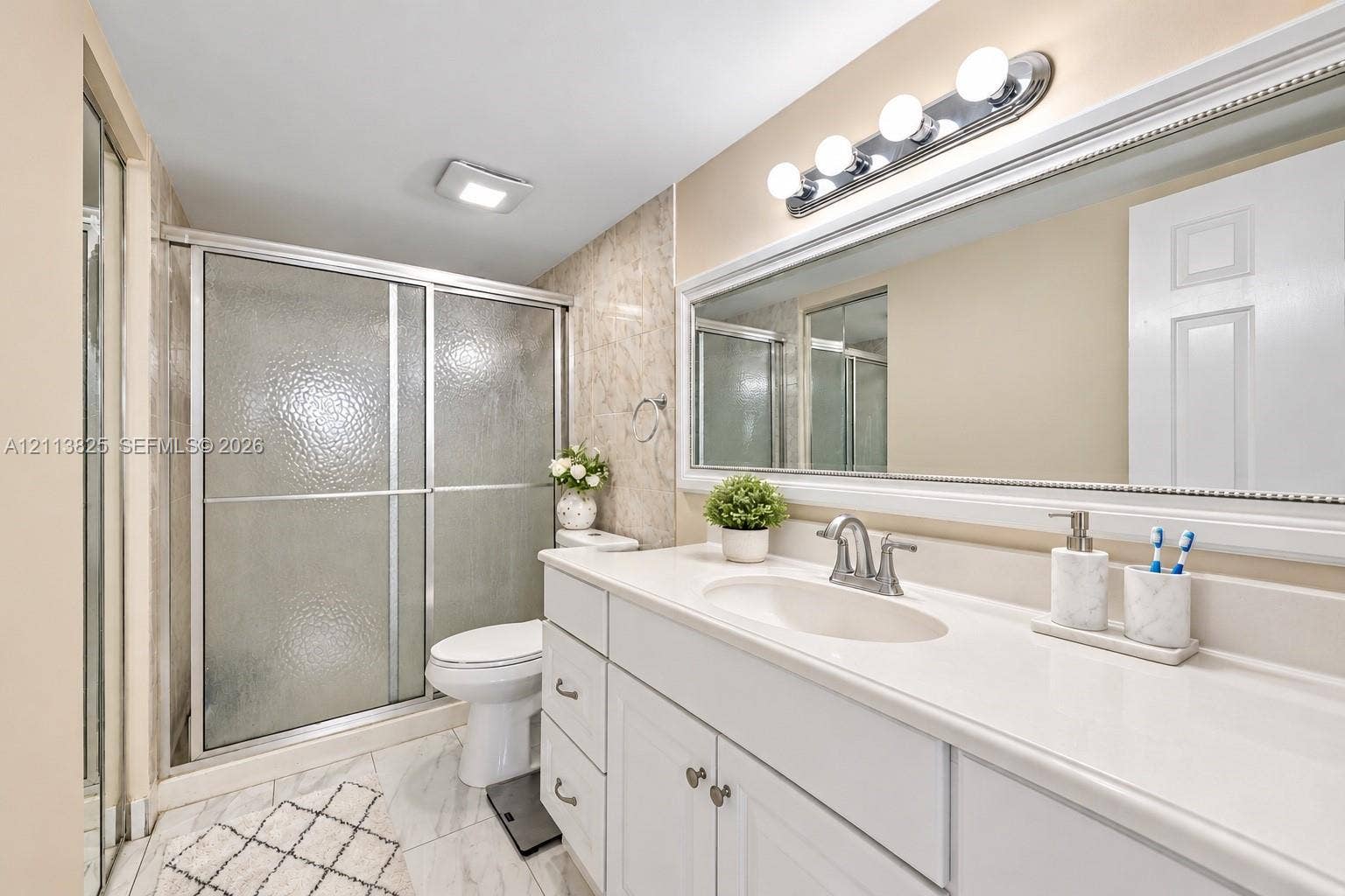 1200 NW 80th Avenue, #405A, Margate, FL 33063 Bathroom featuring a white vanity with a solid-surface countertop, an integrated sink basin, a full-width framed mirror, a glass-enclosed shower with a sliding door, and neutral tile flooring