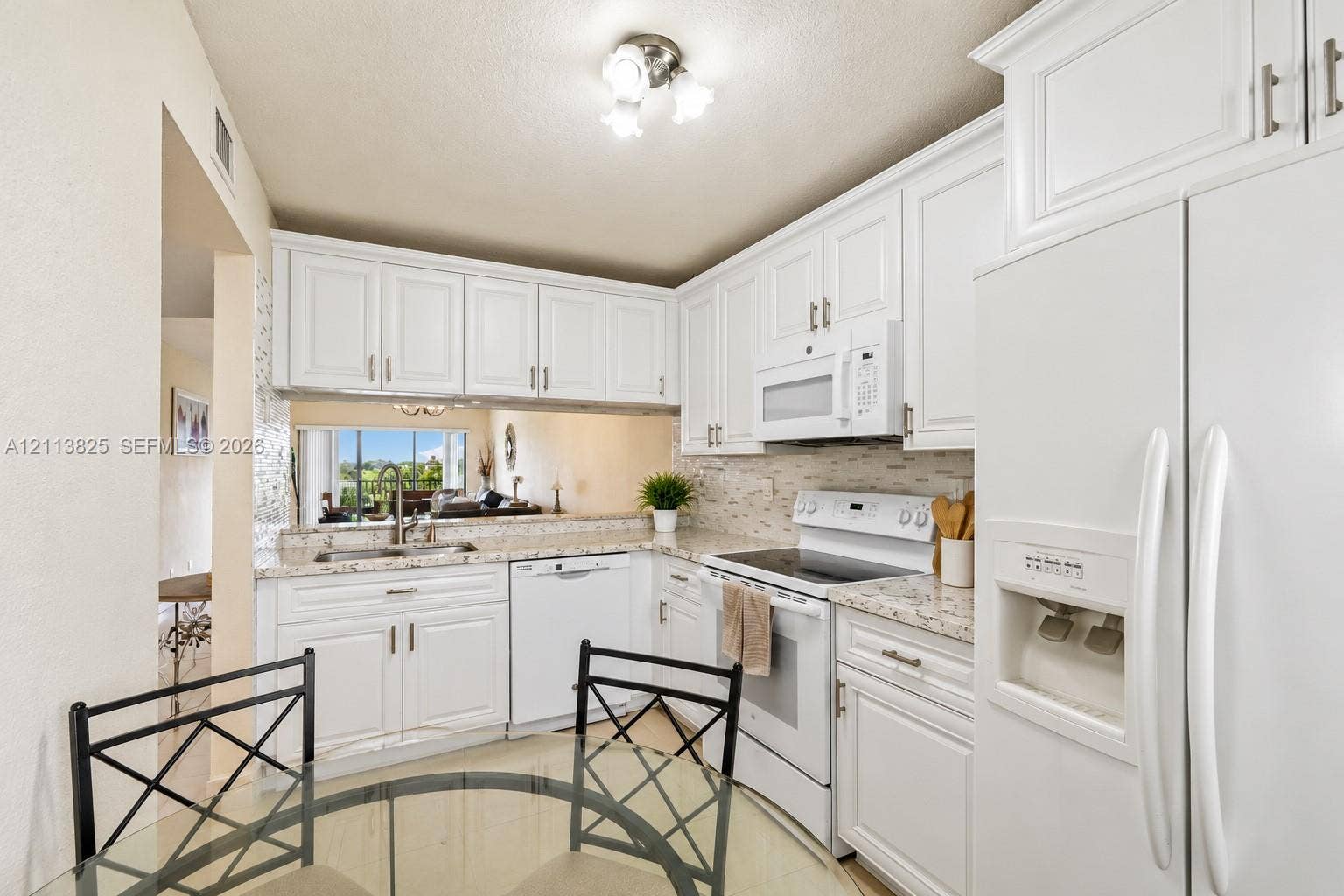 1200 NW 80th Avenue, #405A, Margate, FL 33063 Kitchen featuring white shaker-style cabinetry, stone-finish countertops, tile backsplash, built-in white appliances, and a double-basin stainless steel sink