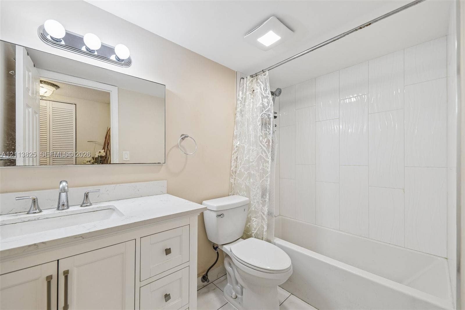 1200 NW 80th Avenue, #405A, Margate, FL 33063 Bathroom featuring a vanity with a light-toned countertop, integrated rectangular sink, wall-mounted mirror, polished chrome lighting, and a bathtub with white vertical-stacked wall tile