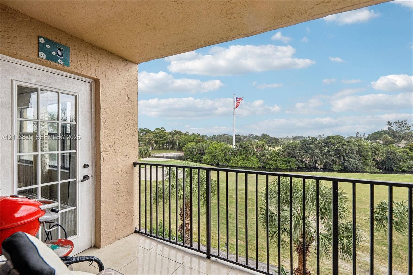 1200 NW 80th Avenue, #405A, Margate, FL 33063 Covered balcony featuring tile flooring and a black metal railing overlooking a golf course with mature palm trees