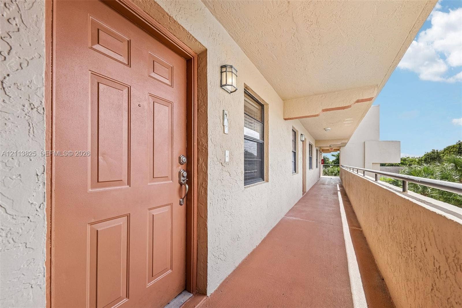 1200 NW 80th Avenue, #405A, Margate, FL 33063 Exterior entry featuring a raised-panel door, textured stucco wall finishes, metal safety railing, and wall-mounted exterior lighting