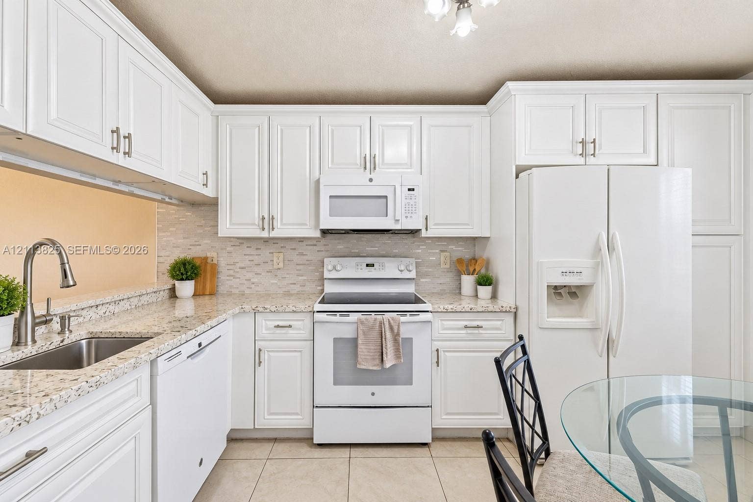 1200 NW 80th Avenue, #405A, Margate, FL 33063 Kitchen featuring white shaker-style cabinetry, speckled stone-finish countertops, a subway-patterned tile backsplash, stainless steel under-mount sink with a high-arch faucet, and white appliances