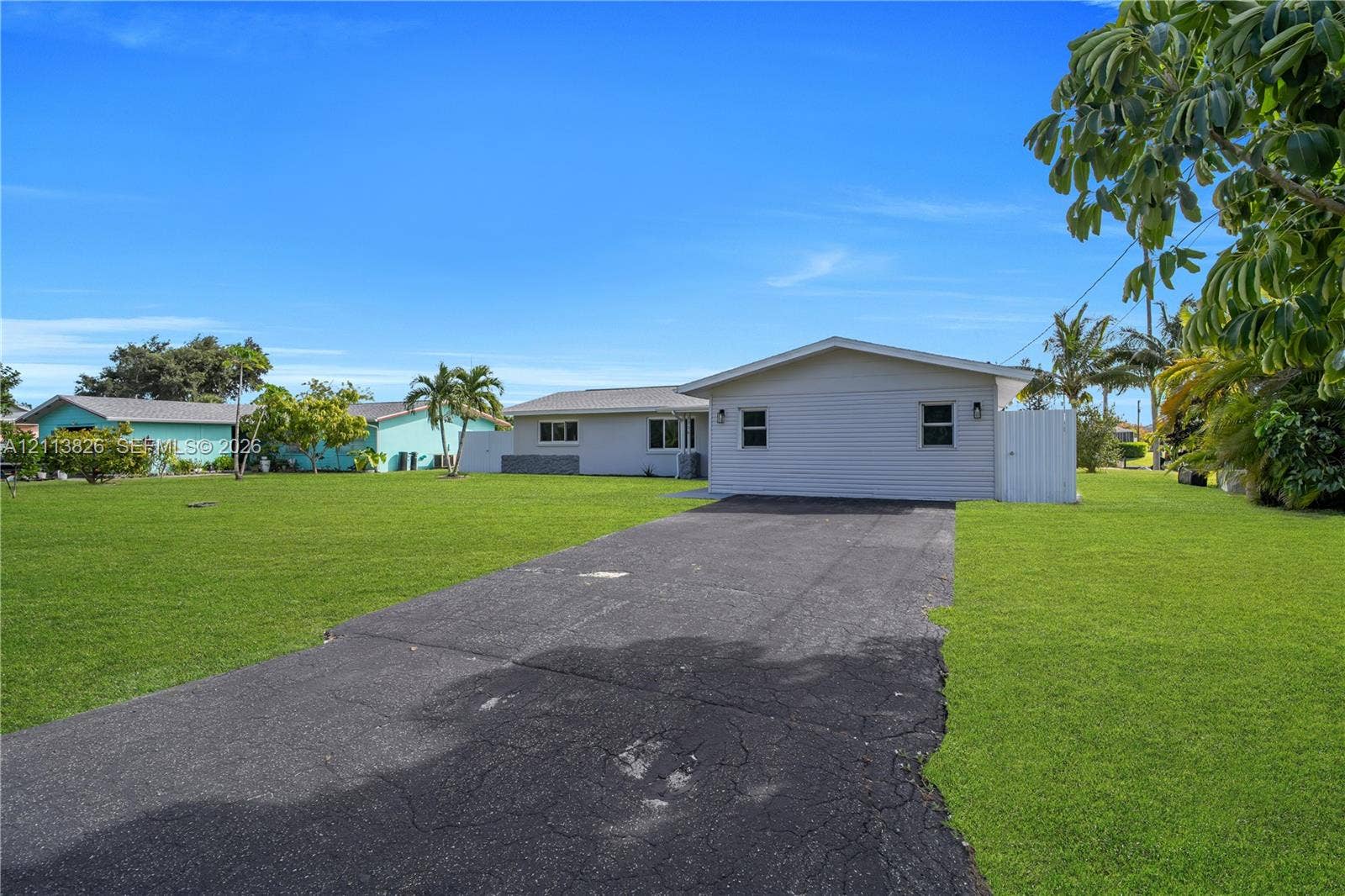 1206 NE 4th Terrace, Cape Coral, Cape Coral, FL 33909 Single-story residence featuring light-colored horizontal siding, a pitched roof, an asphalt driveway, and a expansive grassy lawn