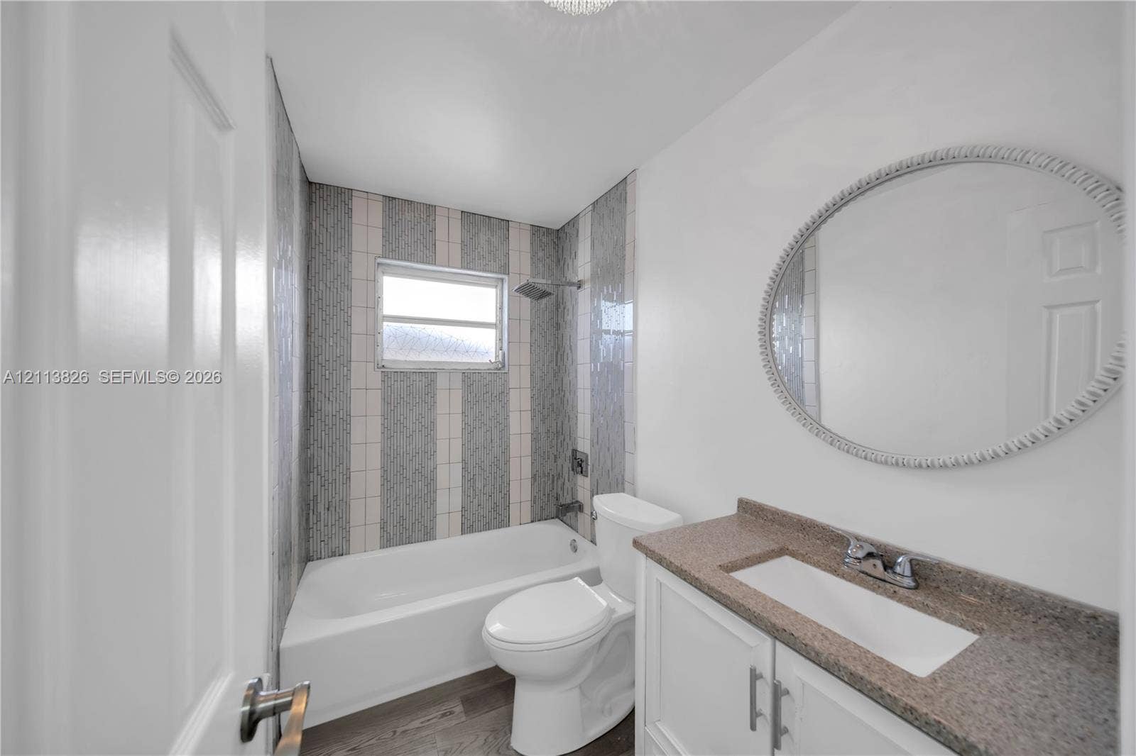 1206 NE 4th Terrace, Cape Coral, Cape Coral, FL 33909 Bathroom featuring a vanity with stone-finish countertop, oval wall-mounted mirror, white tub, and vertical tile shower surround