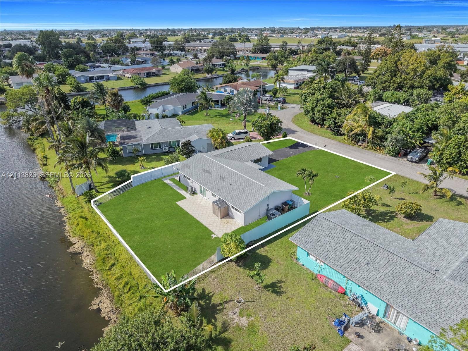 1206 NE 4th Terrace, Cape Coral, Cape Coral, FL 33909 Waterfront property featuring a concrete patio, perimeter fencing, and an expansive lawn
