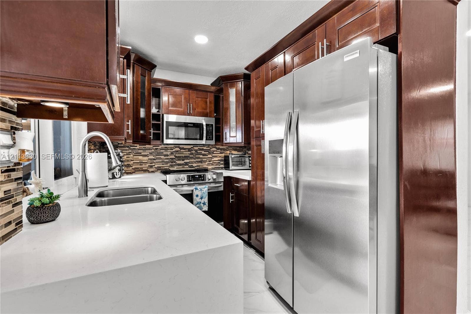 3545 SW 104th Court, Miami, FL 33165 Kitchen featuring stained wood cabinetry, quartz countertops, a multi-tone tile backsplash, stainless steel appliances, and a double-basin undermount sink