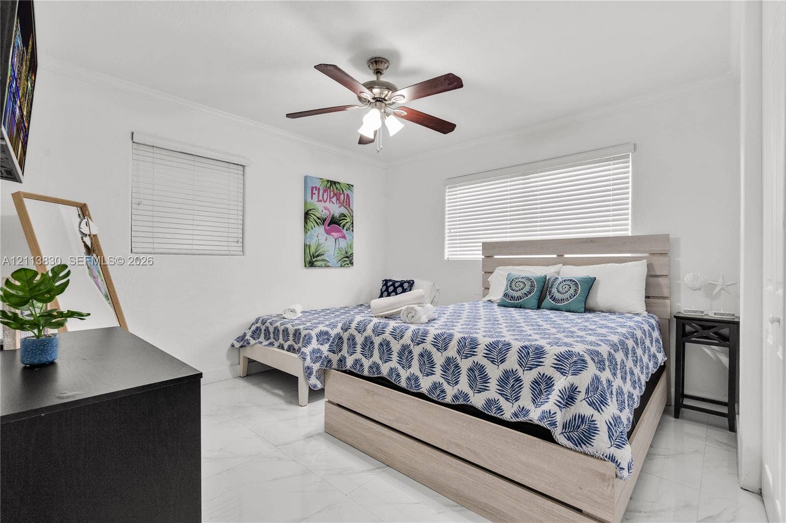 3545 SW 104th Court, Miami, FL 33165 Neutral-toned interior space featuring light-colored stone-finish flooring, two large windows with horizontal blinds, and a multi-blade ceiling fan with an integrated light fixture