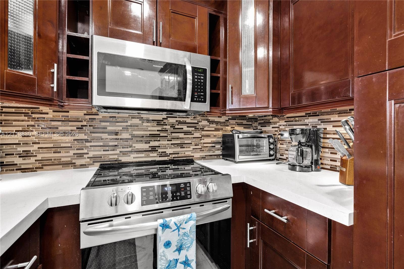 3545 SW 104th Court, Miami, FL 33165 Kitchen featuring dark-finish wood cabinetry, quartz countertops, multi-toned horizontal glass tile backsplash, and stainless steel appliances including a gas range and over-the-range microwave