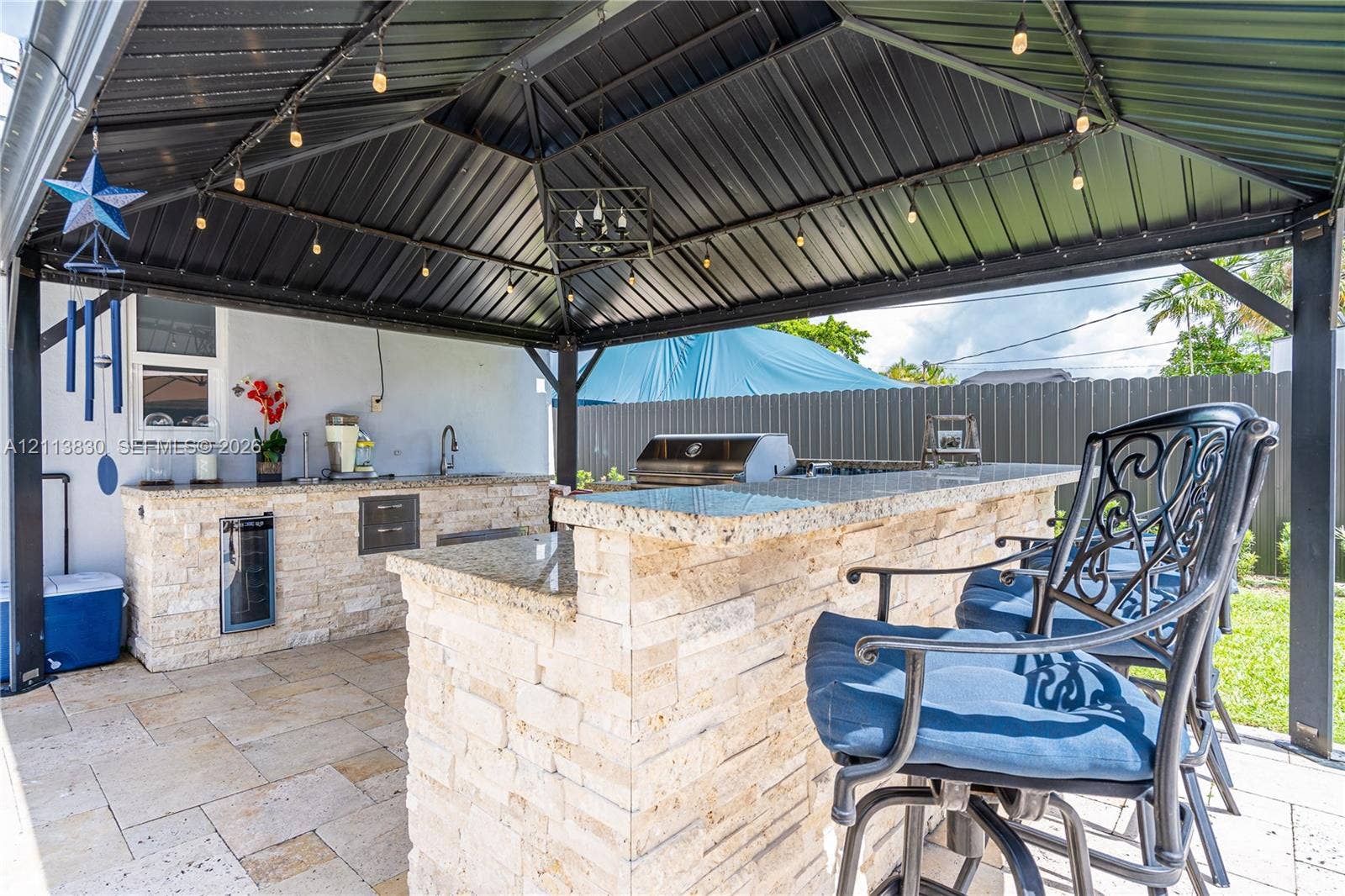 3545 SW 104th Court, Miami, FL 33165 Covered outdoor kitchen featuring a stone-clad bar, natural stone countertop, built-in beverage refrigerator, and metal gazebo structure