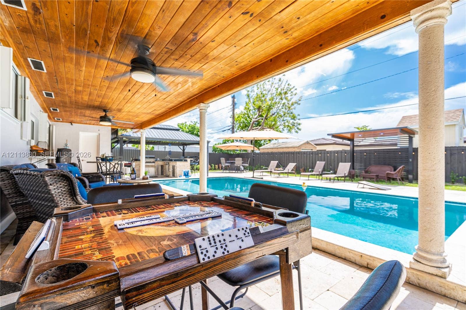 3545 SW 104th Court, Miami, FL 33165 Covered patio featuring a stained wood plank ceiling, recessed lighting, and structural columns overlooking a rectangular swimming pool with paved decking and a built-in outdoor kitchen
