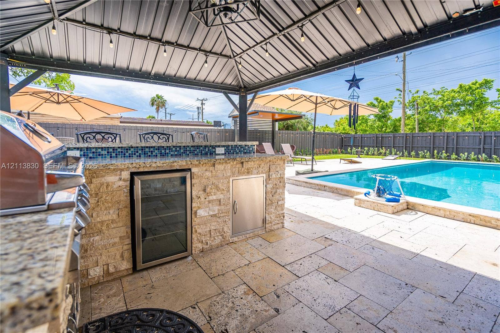 3545 SW 104th Court, Miami, FL 33165 Covered outdoor kitchen featuring stone veneer, integrated stainless steel appliances, and stone-finish countertops, paired with a pool and paved patio