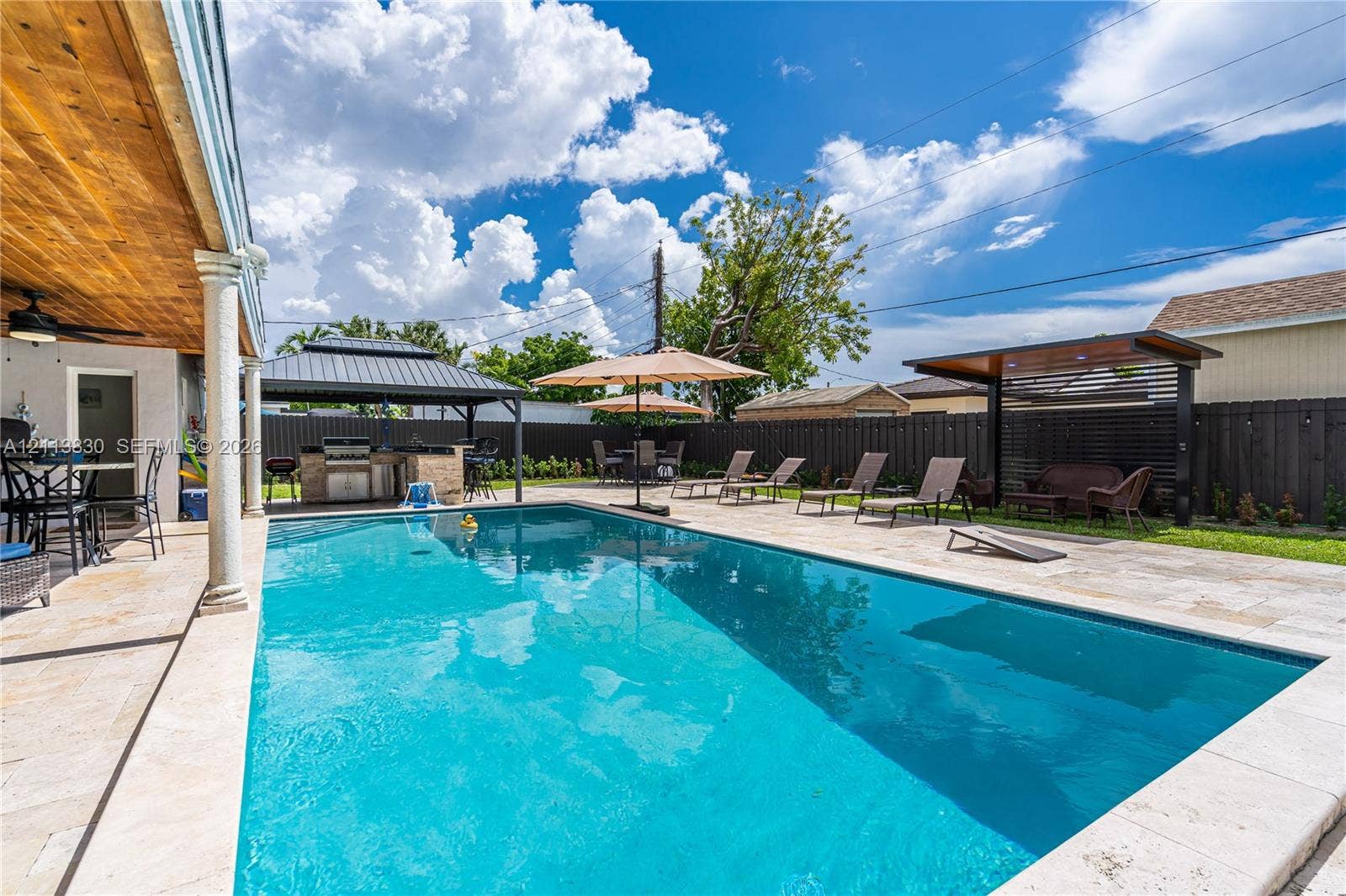 3545 SW 104th Court, Miami, FL 33165 Outdoor area featuring an in-ground swimming pool, stone paver decking, covered patio with wood-paneled ceiling, and a built-in outdoor kitchen with a metal-roof gazebo
