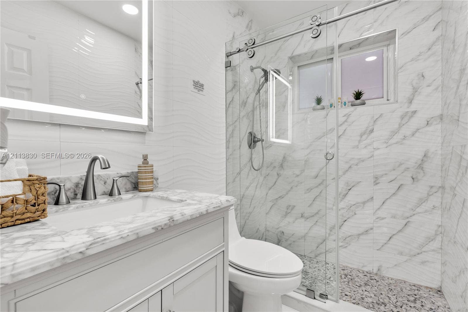 3545 SW 104th Court, Miami, FL 33165 Bathroom featuring a vanity with stone-top basin, integrated LED-backlit mirror, wall-mounted faucet, and glass-enclosed shower with tiled surround and textured flooring