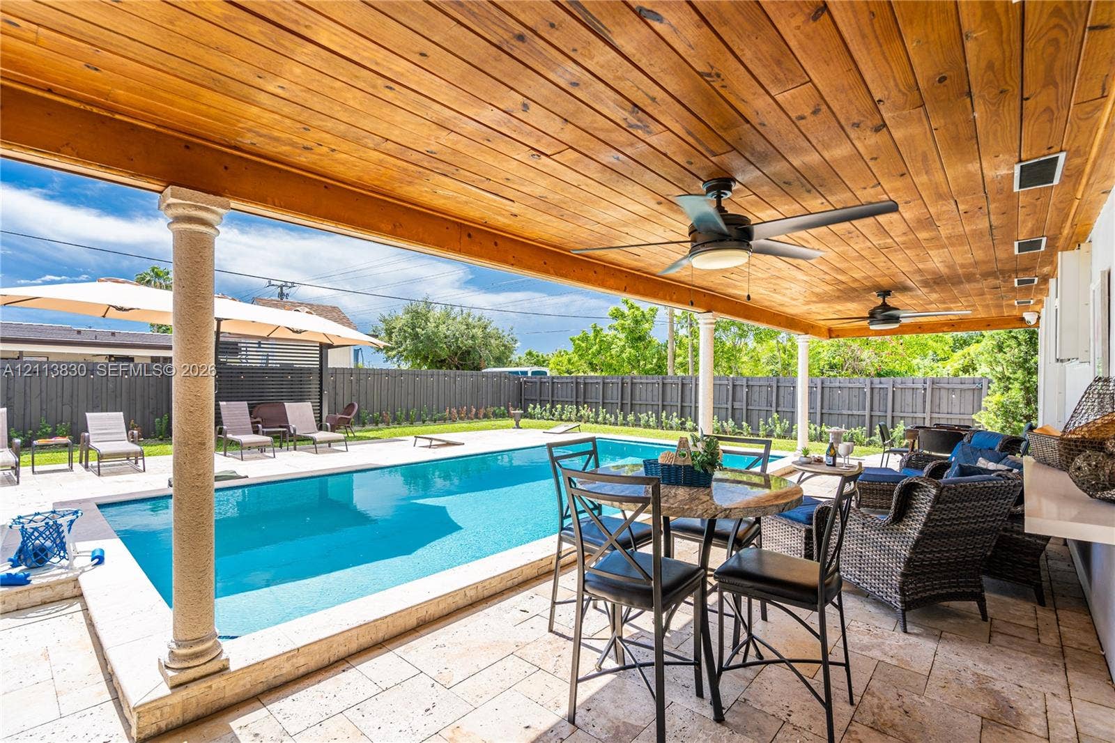 3545 SW 104th Court, Miami, FL 33165 Covered patio featuring a stained wood plank ceiling, dual ceiling fans, stone paver decking, and an in-ground swimming pool with a stone coping border