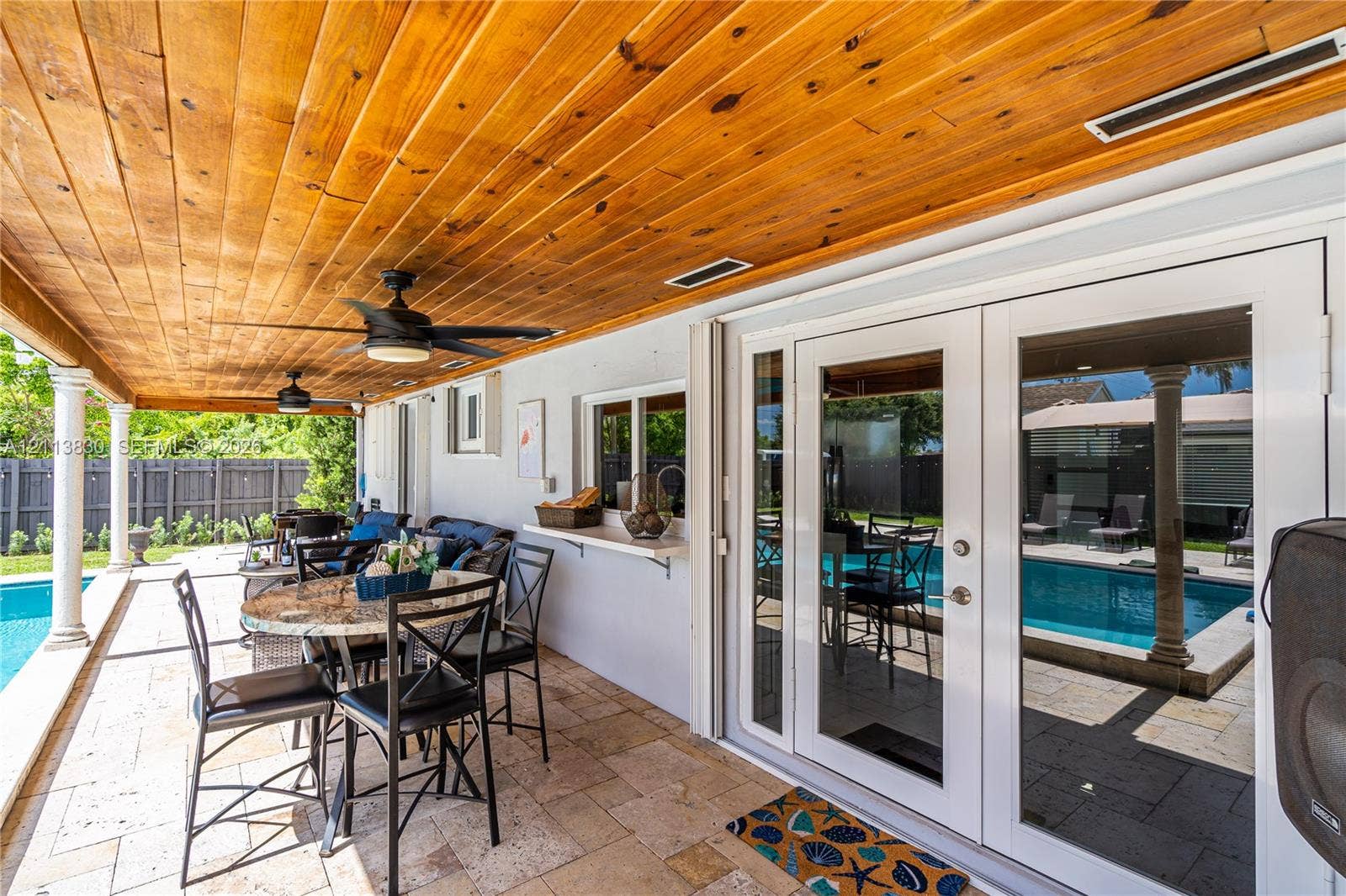 3545 SW 104th Court, Miami, FL 33165 Covered patio featuring a wood-plank ceiling, natural stone tile flooring, ceiling fans, built-in pass-through service shelf, and French doors