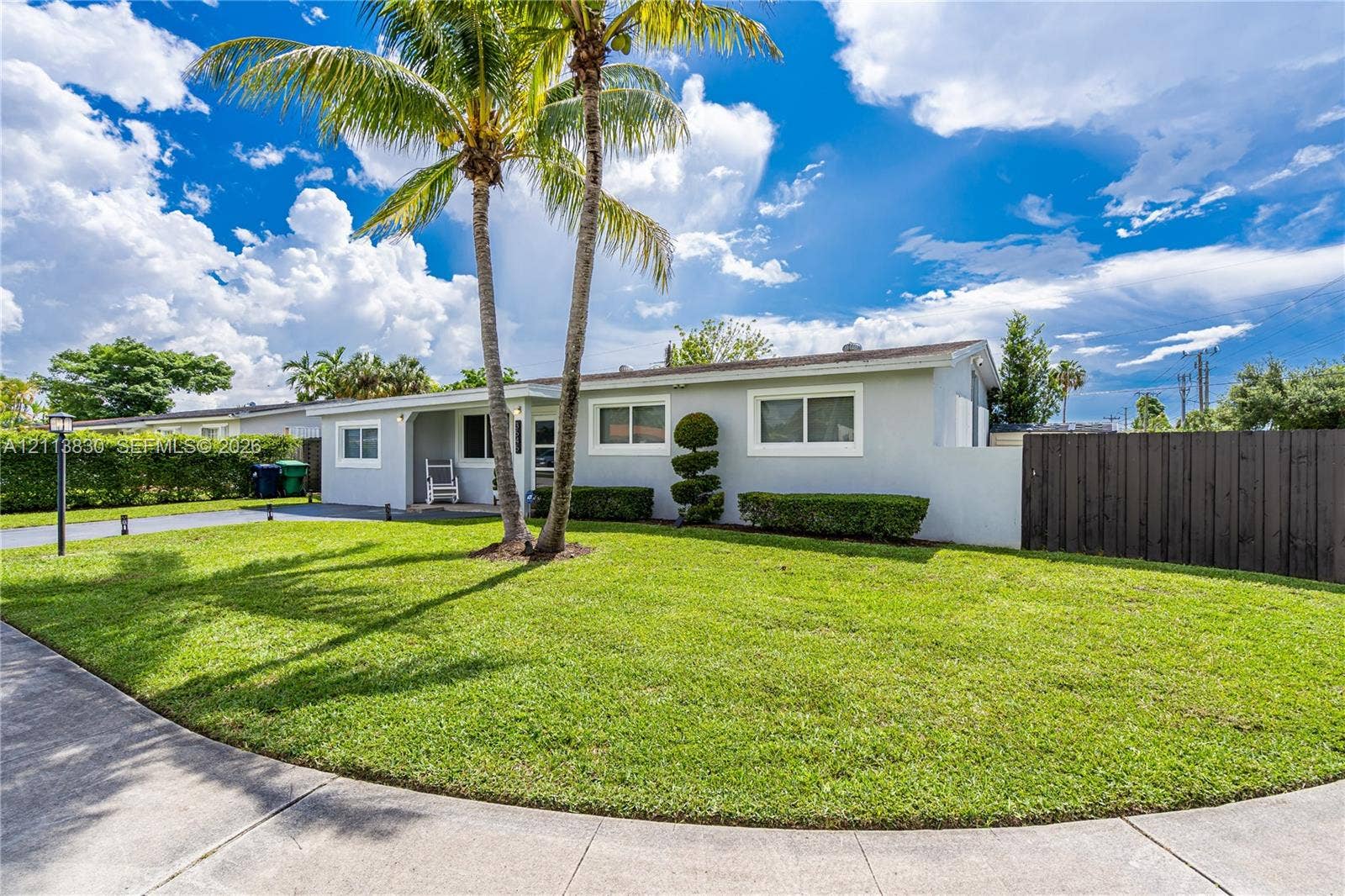 3545 SW 104th Court, Miami, FL 33165 Single-story exterior featuring a light-toned smooth finish, manicured lawn, tall palm trees, and tall wood fencing