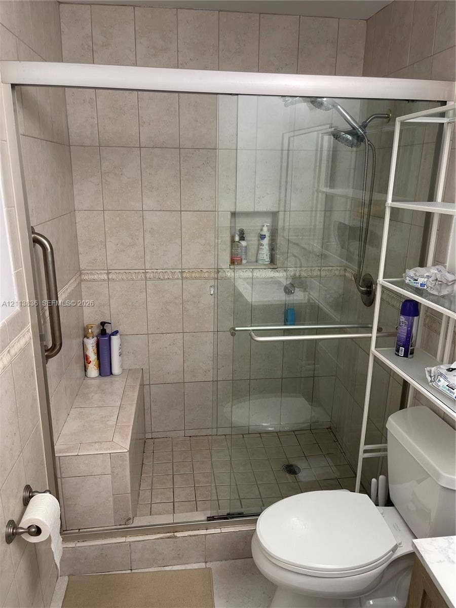 10153 SW 51st Street, Cooper City, Cooper City, FL 33328 Walk-in shower featuring tile surround, integrated tiled bench, glass sliding enclosure, built-in recessed wall niche, and handheld shower fixture