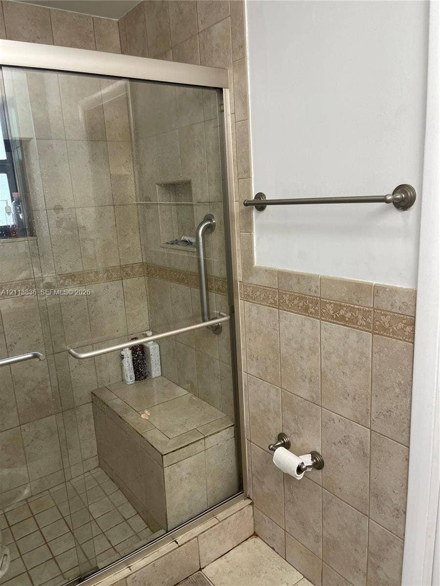 10153 SW 51st Street, Cooper City, Cooper City, FL 33328 Walk-in shower featuring a tiled built-in bench, glass sliding enclosure, integrated wall niche, metal grab bar, and neutral-toned wall tiling with decorative trim