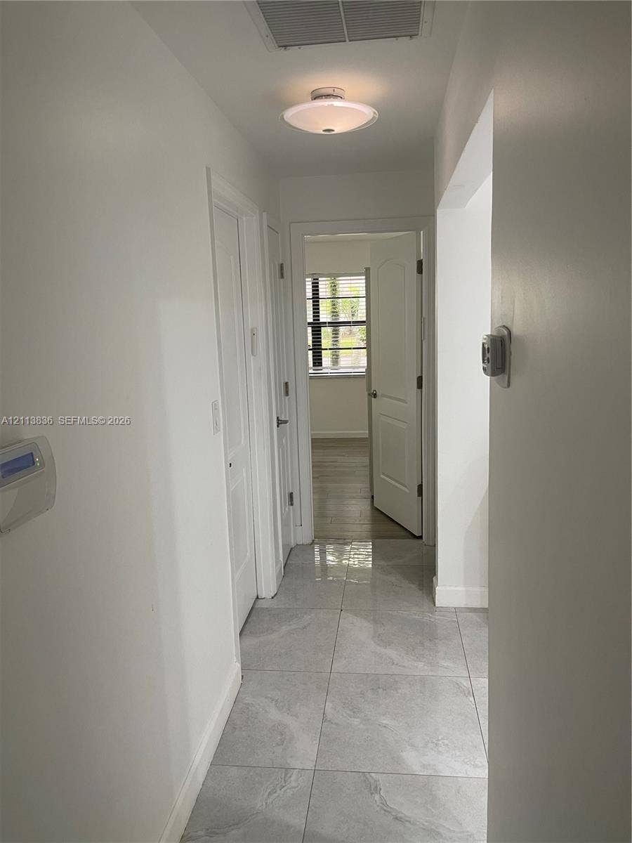 10153 SW 51st Street, Cooper City, Cooper City, FL 33328 Interior hallway featuring large-format ceramic tile flooring, neutral wall finishes, semi-flush mount ceiling lighting, and multi-panel interior doors