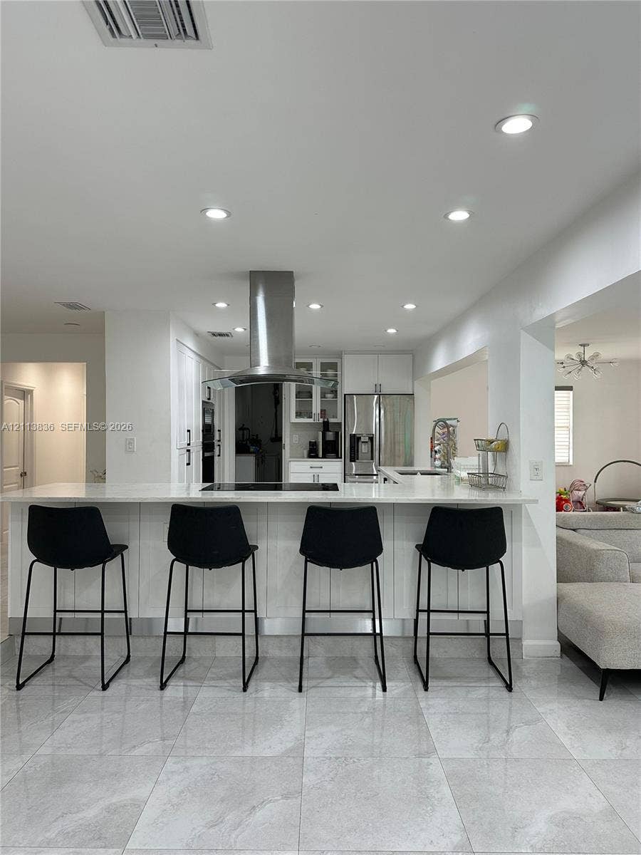 10153 SW 51st Street, Cooper City, Cooper City, FL 33328 Kitchen featuring white cabinetry, an expansive waterfall-edge peninsula with stone-finish countertops, stainless steel appliances, a chimney-style range hood, and large-format tile flooring
