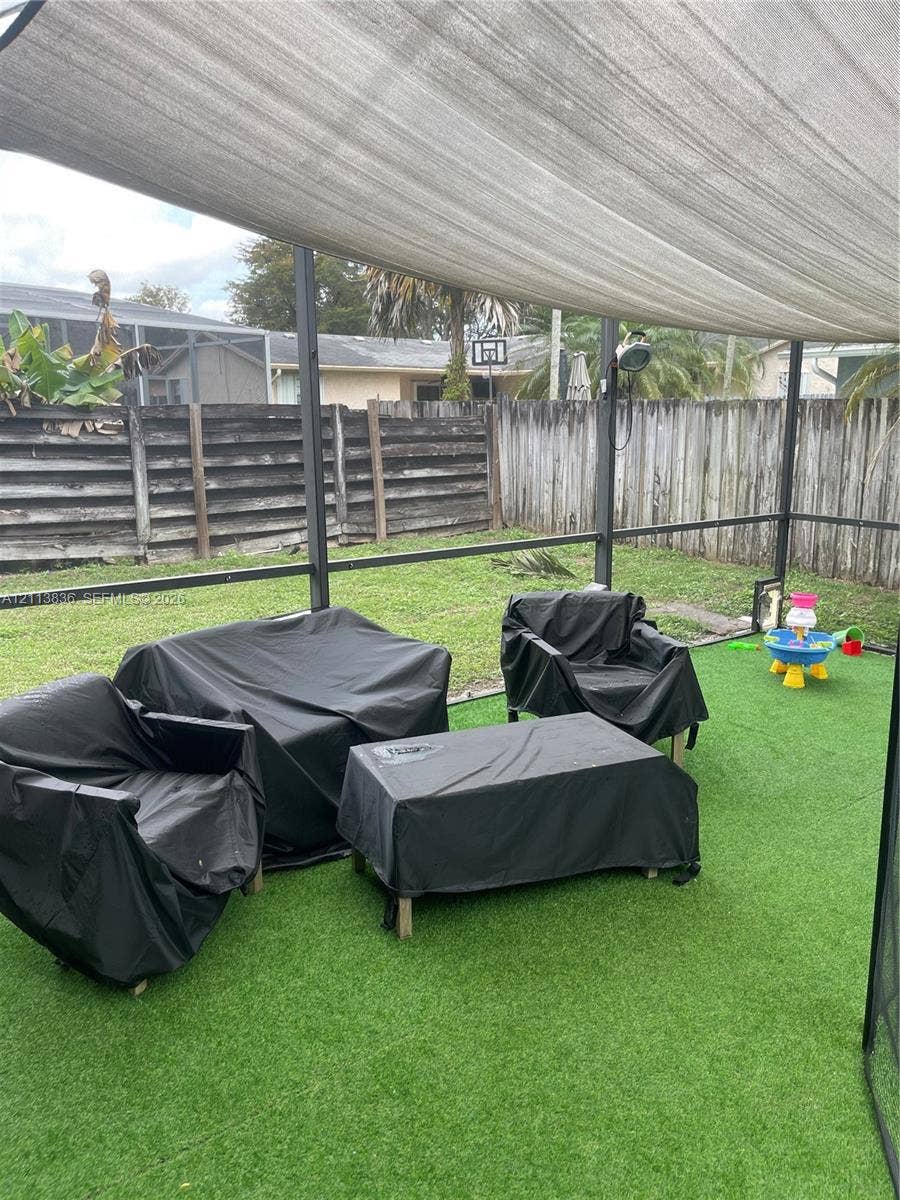 10153 SW 51st Street, Cooper City, Cooper City, FL 33328 Screened-in patio featuring artificial turf, a permanent fabric sun shade, and wood-paneled privacy fencing