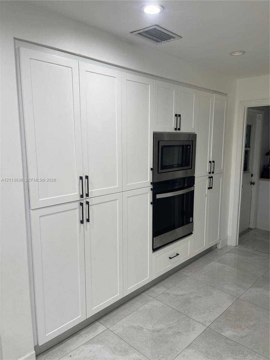 10153 SW 51st Street, Cooper City, Cooper City, FL 33328 Full-height white cabinetry with Shaker-style doors, matte black hardware, recessed lighting, stainless steel built-in double oven and microwave, and large-format porcelain tile flooring