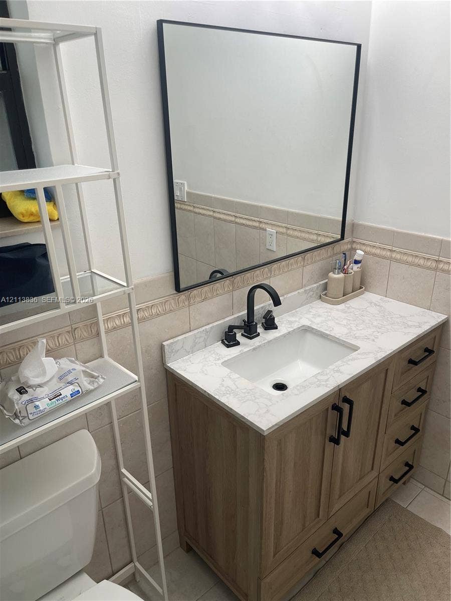 10153 SW 51st Street, Cooper City, Cooper City, FL 33328 Vanity featuring wood-finish cabinetry, a stone-patterned countertop, integrated basin, matte black faucet, and a rectangular mirror with a black frame