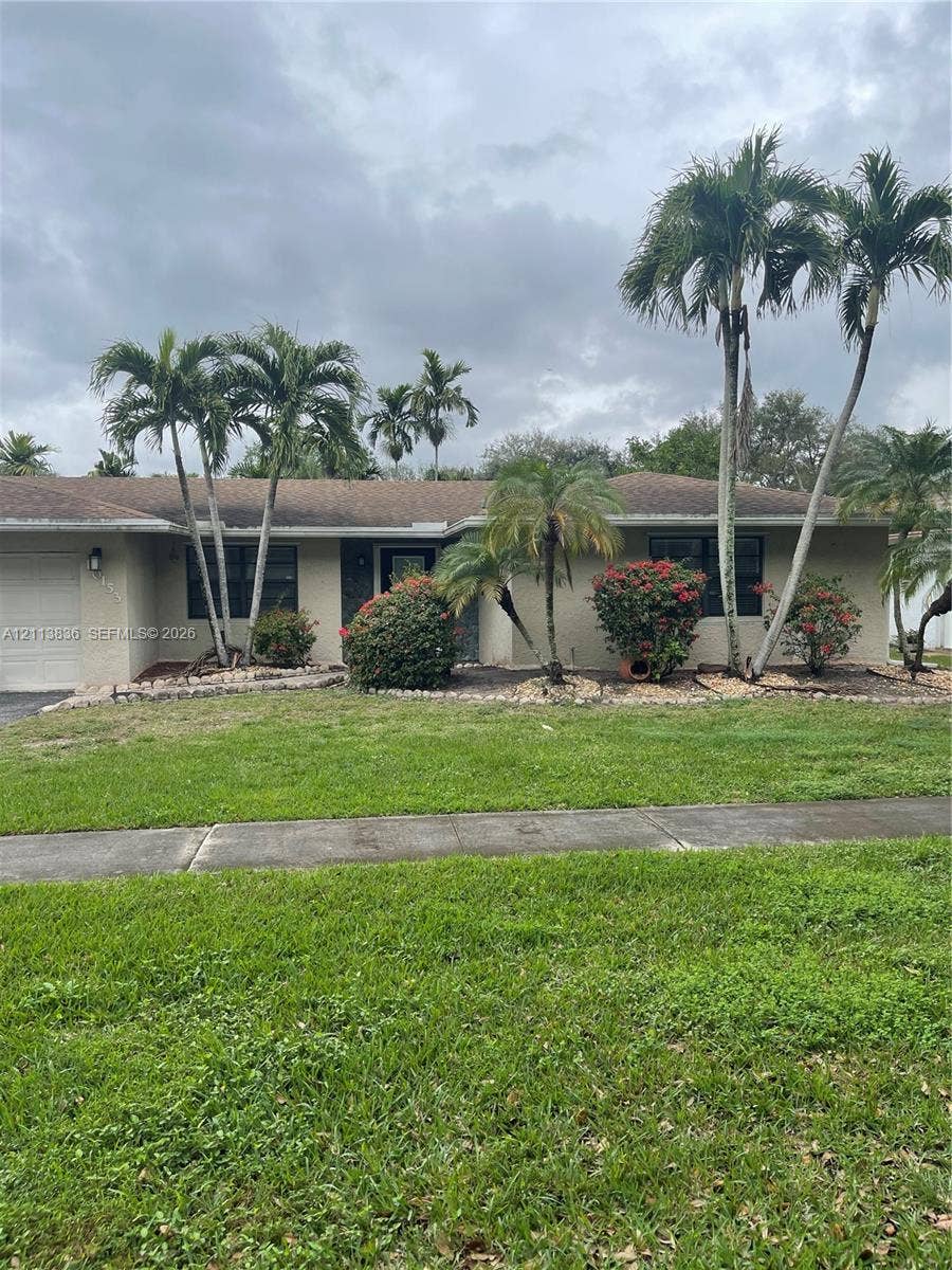 10153 SW 51st Street, Cooper City, Cooper City, FL 33328 Single-story exterior featuring a stucco facade, attached garage, manicured lawn, stone landscaping beds, and mature palm trees