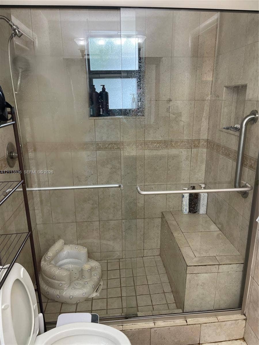 10153 SW 51st Street, Cooper City, Cooper City, FL 33328 Walk-in shower enclosure featuring floor-to-ceiling tile, a built-in bench seat, a recessed wall niche, and a glass sliding door