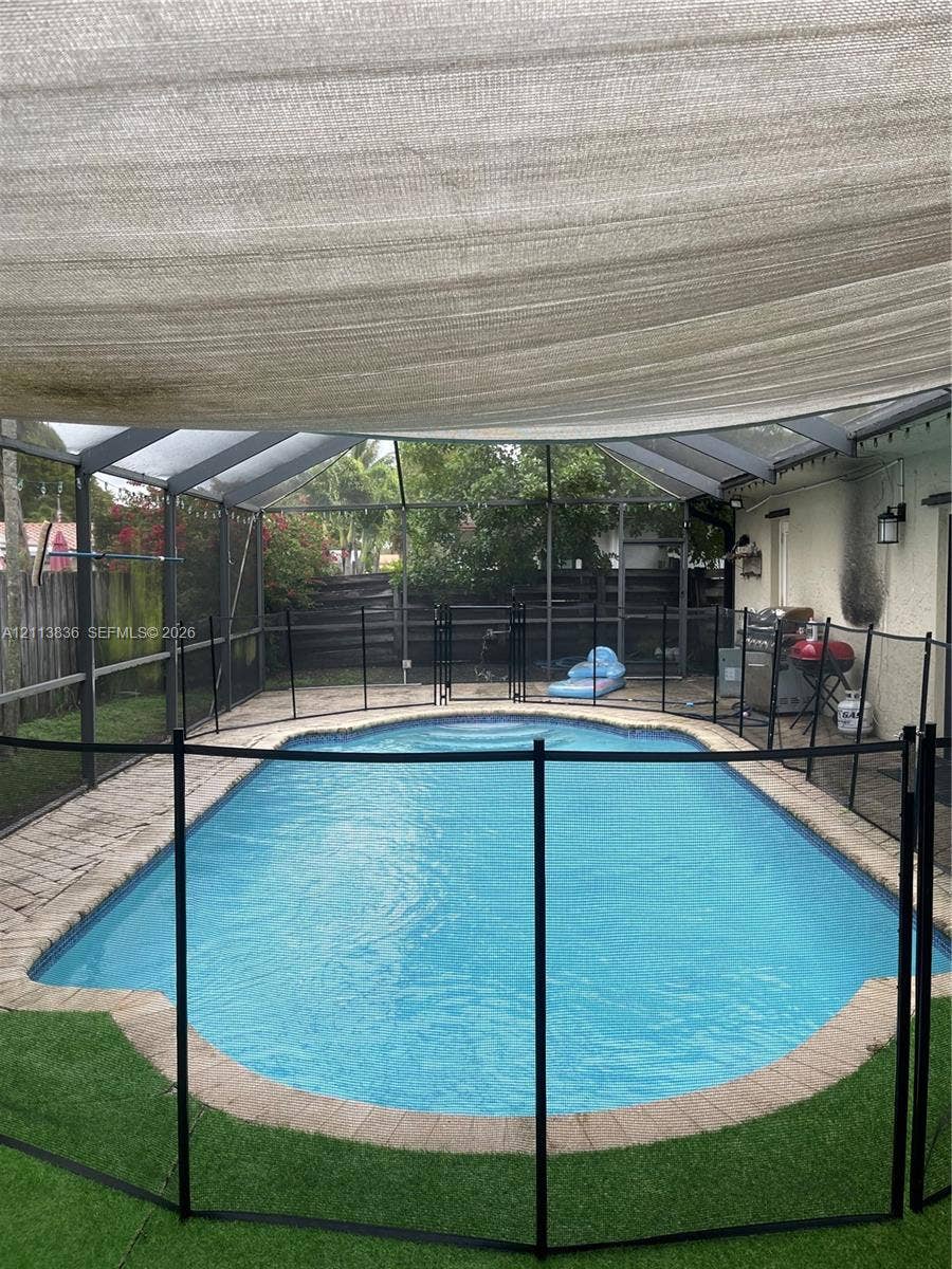 10153 SW 51st Street, Cooper City, Cooper City, FL 33328 Screen-enclosed swimming pool featuring a paved perimeter, removable safety fencing, and an overhead shade canopy
